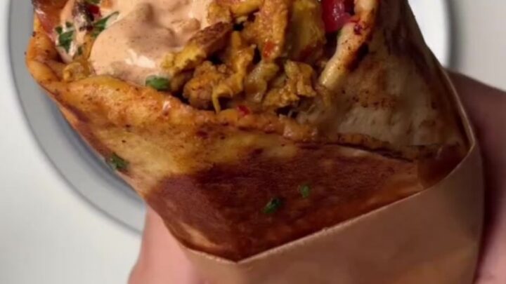 Crispy chicken shawarma wrap cut diagonally, showing melted cheese and pickles, with garlic sauce on the side.