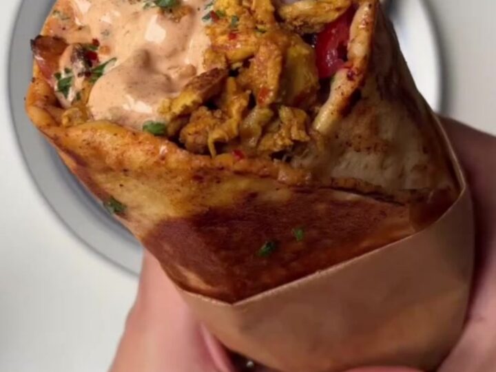 Crispy chicken shawarma wrap cut diagonally, showing melted cheese and pickles, with garlic sauce on the side.