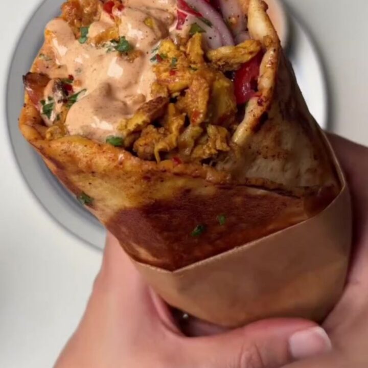 Crispy chicken shawarma wrap cut diagonally, showing melted cheese and pickles, with garlic sauce on the side.
