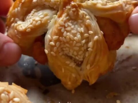Golden crispy sesame cheese pinwheels on a parchment-lined baking sheet, showing flaky layers and melted feta.