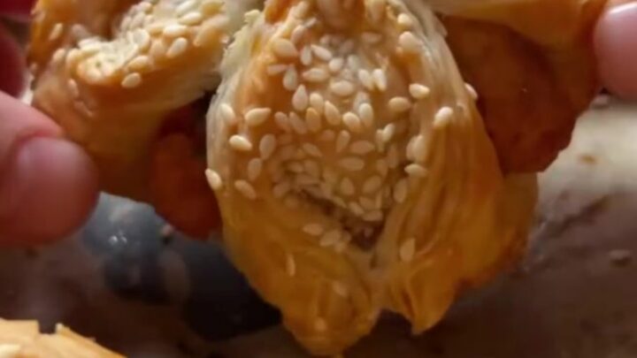 Golden crispy sesame cheese pinwheels on a parchment-lined baking sheet, showing flaky layers and melted feta.