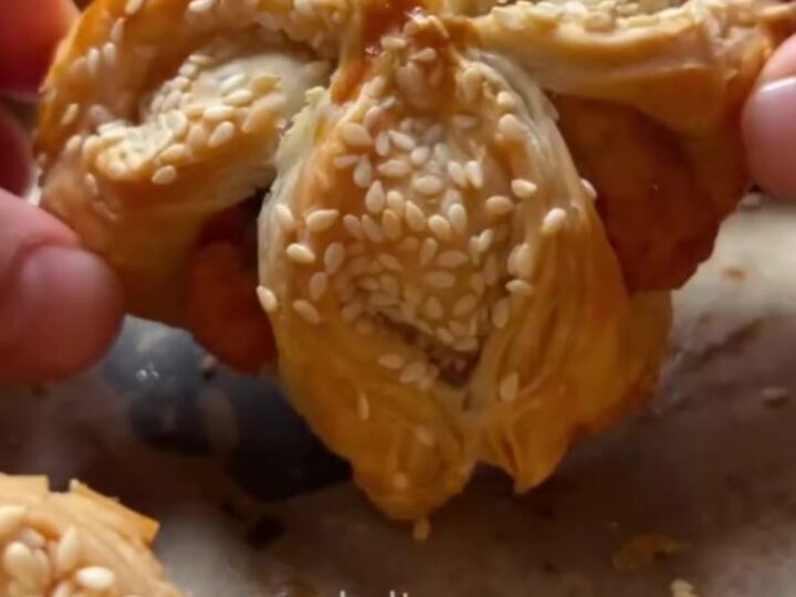 Golden crispy sesame cheese pinwheels on a parchment-lined baking sheet, showing flaky layers and melted feta.