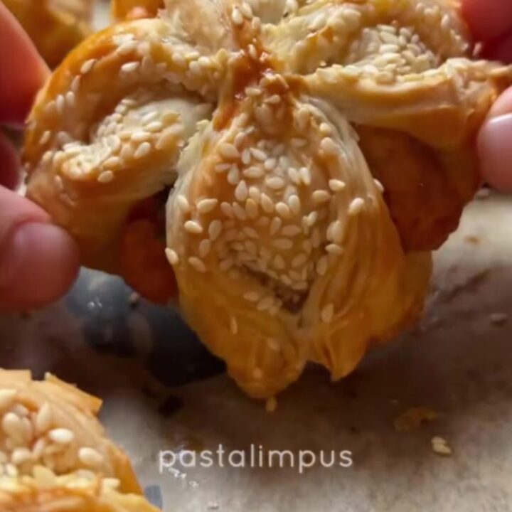 Golden crispy sesame cheese pinwheels on a parchment-lined baking sheet, showing flaky layers and melted feta.