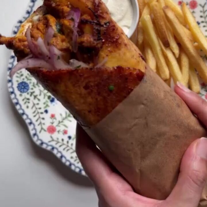 Crispy chicken shawarma wrap cut in half, showing layers of chicken, toum, fries, and pickled turnips