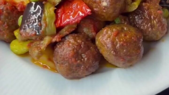 Baking dish with meatballs, eggplant, and peppers in rich tomato sauce, topped with parsley