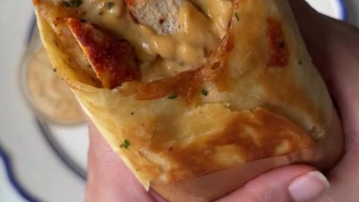 Crispy chicken Alfredo wrap cut in half, showing creamy sauce and melted cheese, with a side of Alfredo sauce for dipping.
