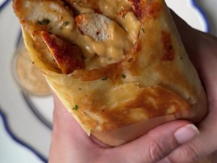 Crispy chicken Alfredo wrap cut in half, showing creamy sauce and melted cheese, with a side of Alfredo sauce for dipping.