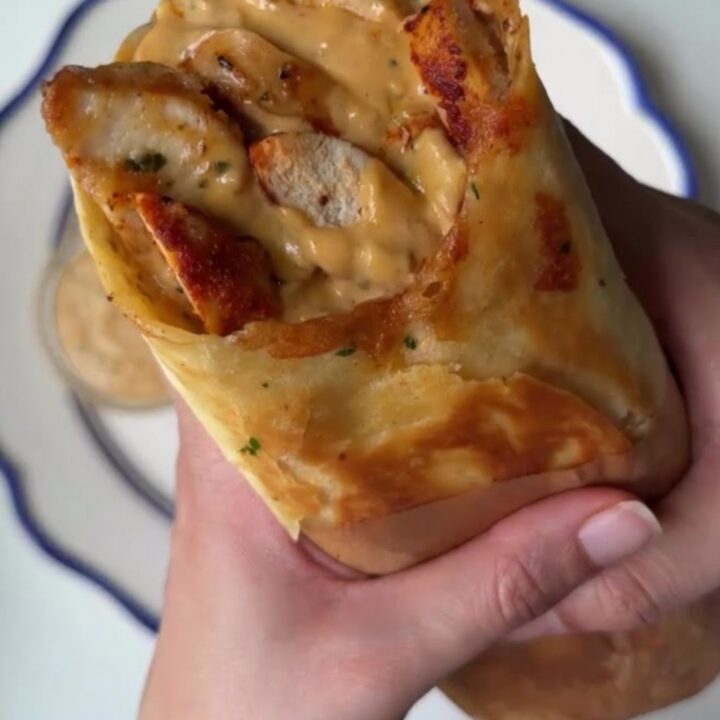Crispy chicken Alfredo wrap cut in half, showing creamy sauce and melted cheese, with a side of Alfredo sauce for dipping.