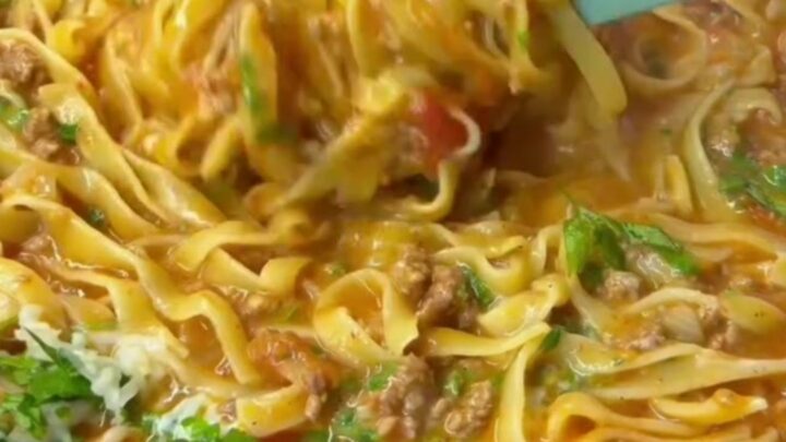 Tagliatelle tossed in beef ragù with melted cheese and basil, served in a wide bowl.