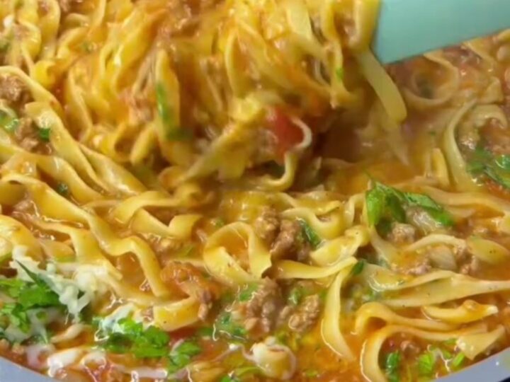 Tagliatelle tossed in beef ragù with melted cheese and basil, served in a wide bowl.
