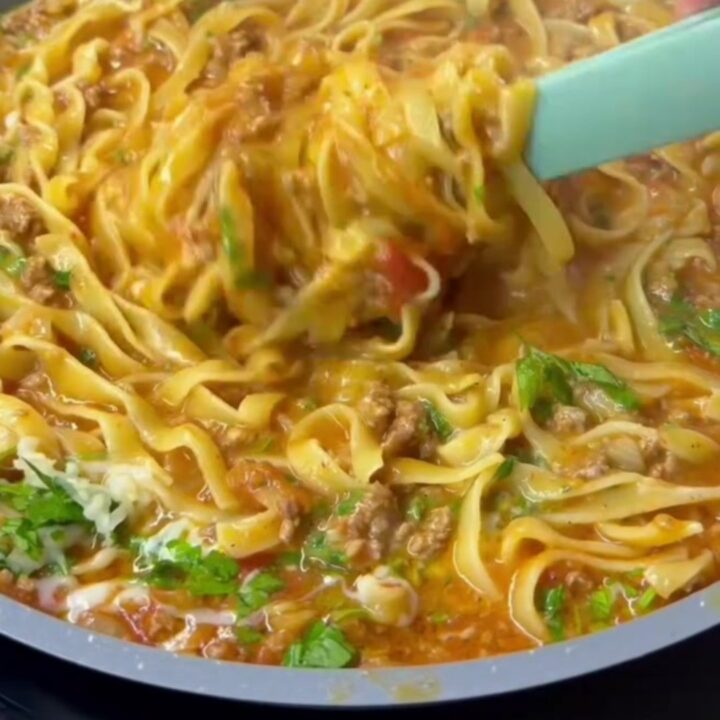 Tagliatelle tossed in beef ragù with melted cheese and basil, served in a wide bowl.