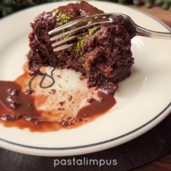 A dark, glossy Turkish wet chocolate cake topped with crushed green pistachios, with a fork lifting a moist slice.