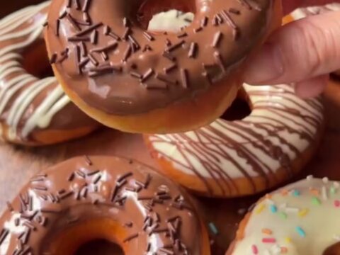 Fluffy ring donuts with glossy milk chocolate glaze and white chocolate spiderweb design on a wire rack