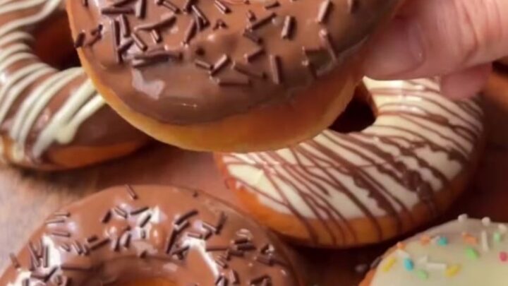 Fluffy ring donuts with glossy milk chocolate glaze and white chocolate spiderweb design on a wire rack