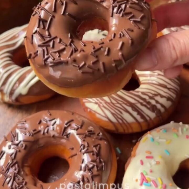 Fluffy ring donuts with glossy milk chocolate glaze and white chocolate spiderweb design on a wire rack