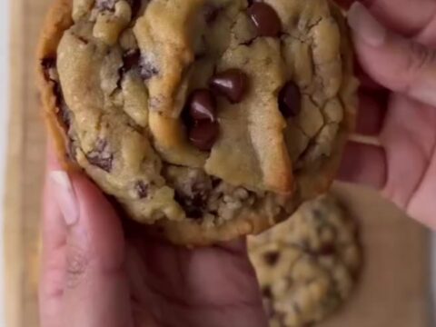 A stack of golden two-chip cookies with crispy edges and melted chocolate chunks, sprinkled with flaky sea salt.
