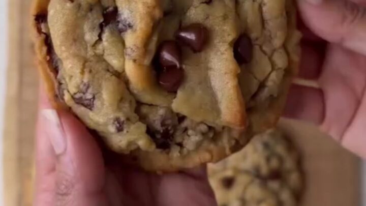 A stack of golden two-chip cookies with crispy edges and melted chocolate chunks, sprinkled with flaky sea salt.
