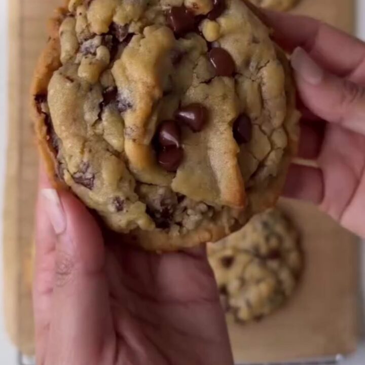 A stack of golden two-chip cookies with crispy edges and melted chocolate chunks, sprinkled with flaky sea salt.