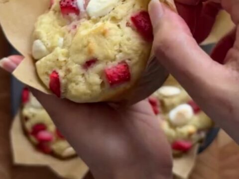 Tall bakery muffins with golden sugar tops, showing a torn open center with strawberries and melted white chocolate