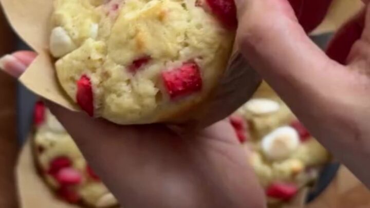 Tall bakery muffins with golden sugar tops, showing a torn open center with strawberries and melted white chocolate