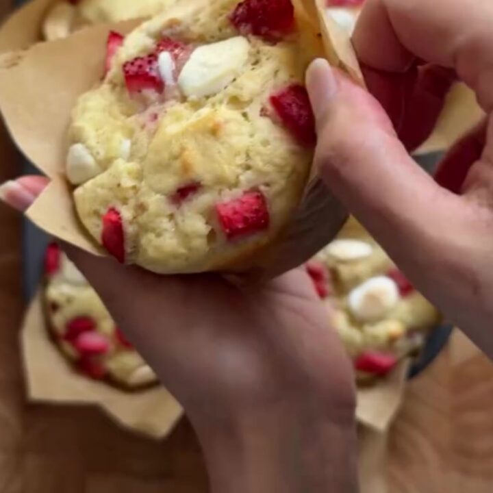 Tall bakery muffins with golden sugar tops, showing a torn open center with strawberries and melted white chocolate