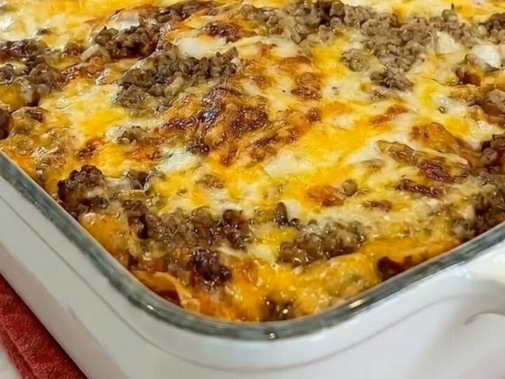 A spatula lifting a generous serving of beef enchilada casserole with a massive molten cheese pull from a white baking dish
