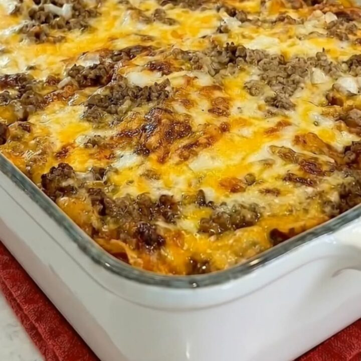 A spatula lifting a generous serving of beef enchilada casserole with a massive molten cheese pull from a white baking dish