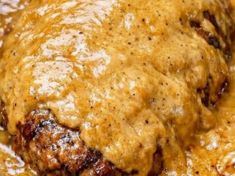 A close-up of tender, shredded beef roast in a thick, velvety golden-brown gravy inside a black slow cooker.