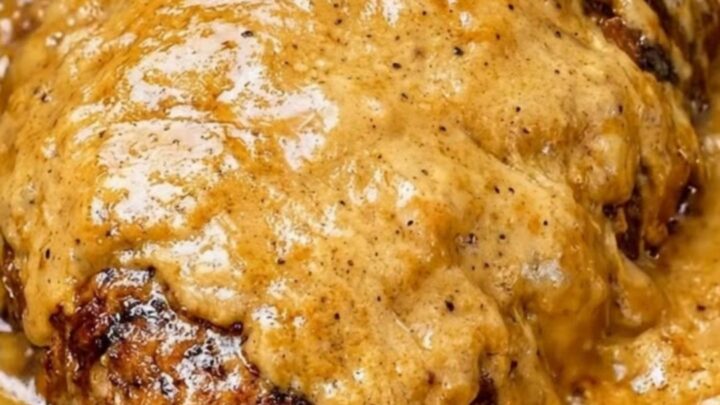 A close-up of tender, shredded beef roast in a thick, velvety golden-brown gravy inside a black slow cooker.
