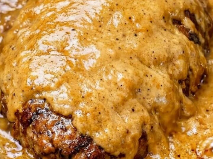 A close-up of tender, shredded beef roast in a thick, velvety golden-brown gravy inside a black slow cooker.