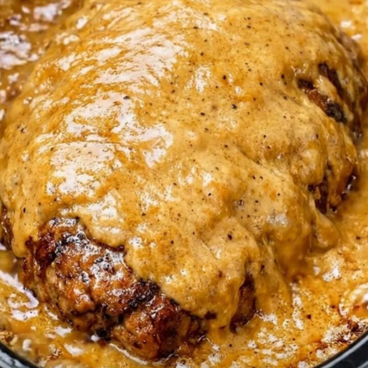 A close-up of tender, shredded beef roast in a thick, velvety golden-brown gravy inside a black slow cooker.