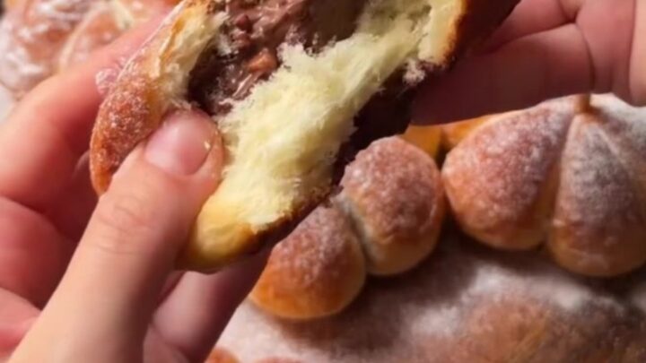 Golden pumpkin-shaped brioche buns with pecan stems on a wooden board, showing melted cheese pull