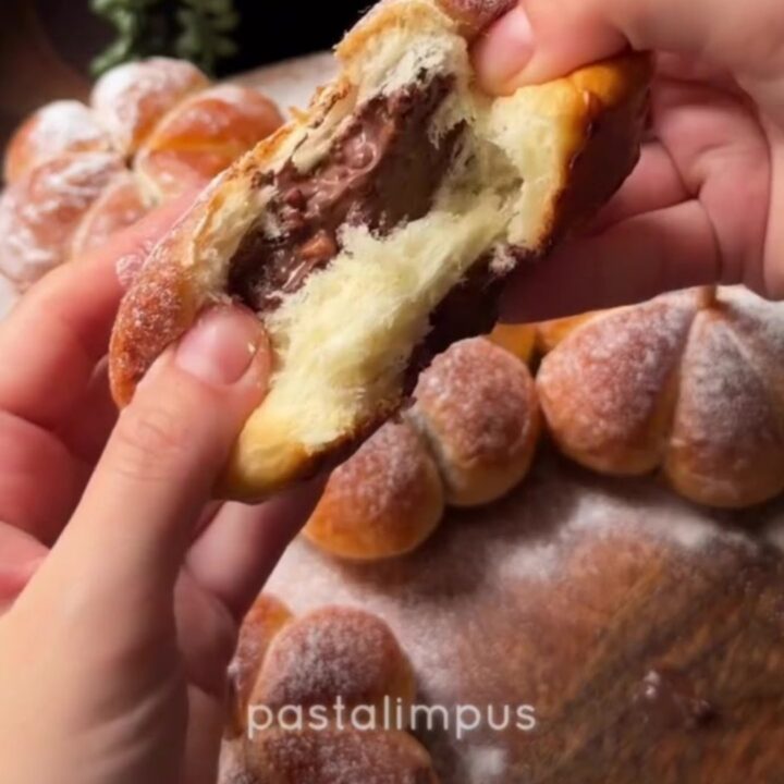 Golden pumpkin-shaped brioche buns with pecan stems on a wooden board, showing melted cheese pull