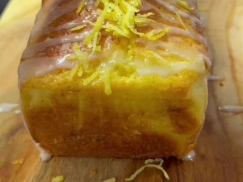Golden whole-lemon loaf cake with glossy white glaze and visible walnut pieces