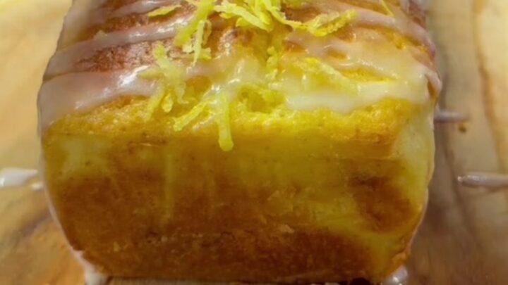 Golden whole-lemon loaf cake with glossy white glaze and visible walnut pieces