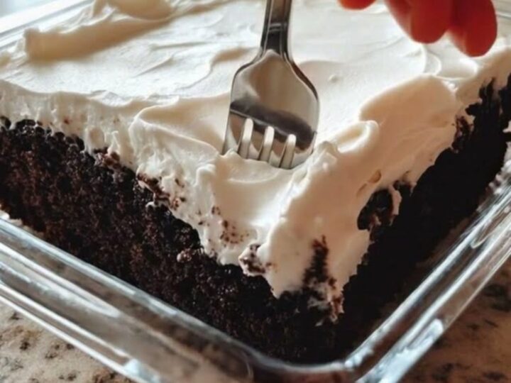 A close-up view of a chocolate sheet cake with fluffy white frosting in a glass dish.
