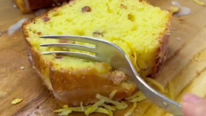 Golden whole-lemon loaf cake with white glaze and lemon zest curls on top