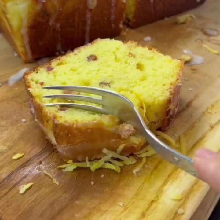 Golden whole-lemon loaf cake with white glaze and lemon zest curls on top