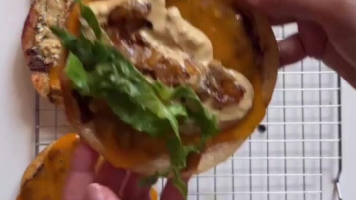 A stack of crispy smash burger tacos with melted cheddar, burger sauce, pickles, and lettuce on a wooden board.