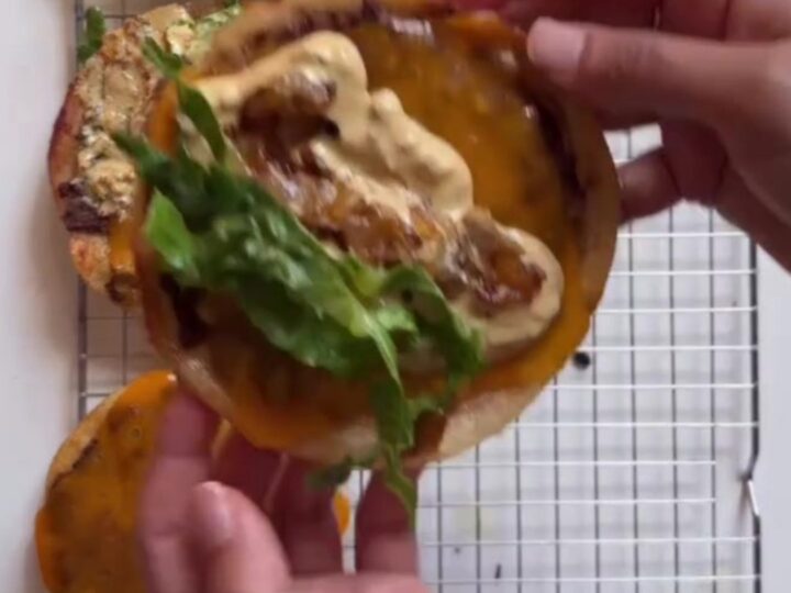 A stack of crispy smash burger tacos with melted cheddar, burger sauce, pickles, and lettuce on a wooden board.