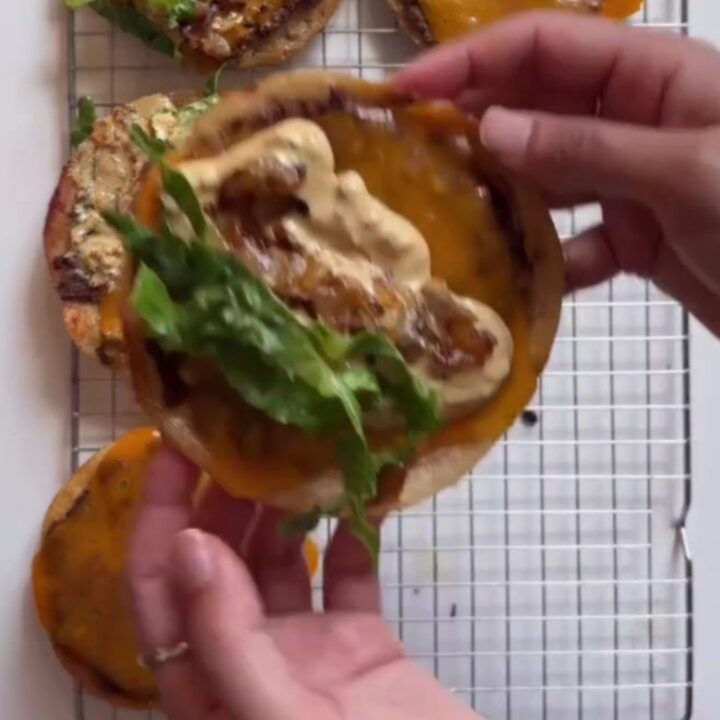 A stack of crispy smash burger tacos with melted cheddar, burger sauce, pickles, and lettuce on a wooden board.