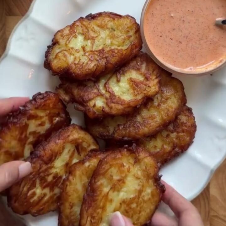 Golden crispy garlic parmesan hashbrowns stacked on a plate with a bowl of spicy mayo for dipping