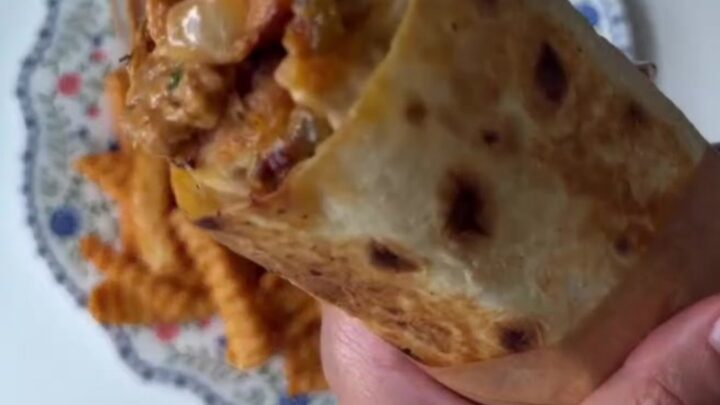 Crispy chicken Philly cheesesteak wrap cut diagonally, showing layers of chicken, peppers, onions