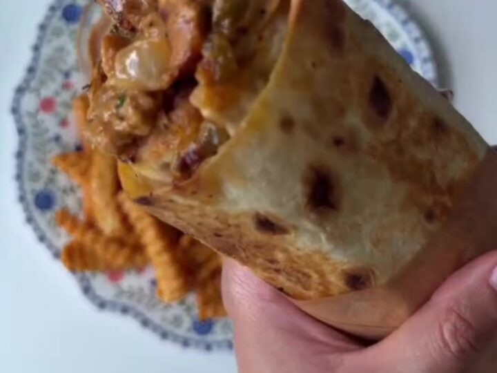 Crispy chicken Philly cheesesteak wrap cut diagonally, showing layers of chicken, peppers, onions