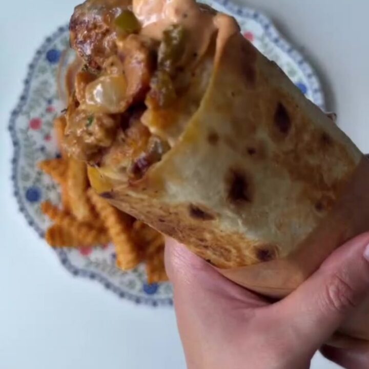 Crispy chicken Philly cheesesteak wrap cut diagonally, showing layers of chicken, peppers, onions