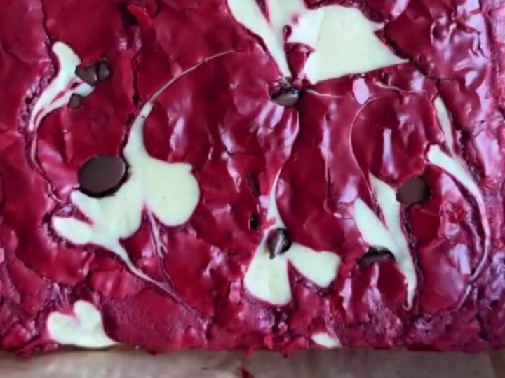 Ultra-fudgy red velvet cheesecake brownies with white cream cheese swirls and dark chocolate chips on top, cut into squares