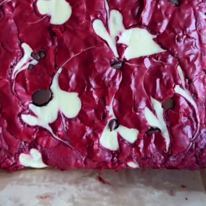 Ultra-fudgy red velvet cheesecake brownies with white cream cheese swirls and dark chocolate chips on top, cut into squares