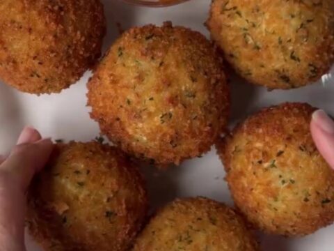 Golden fried potato cheese balls on a plate, with a mozzarella pull stretching from one