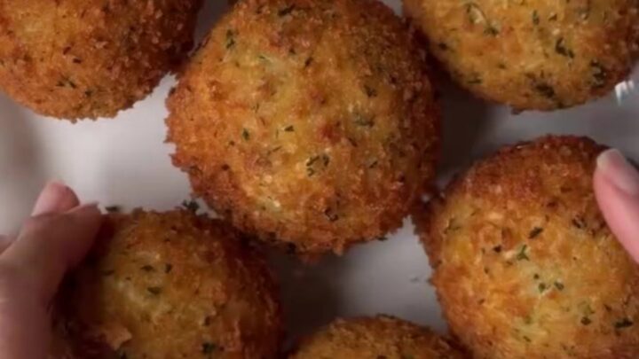 Golden fried potato cheese balls on a plate, with a mozzarella pull stretching from one