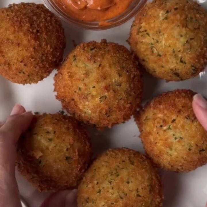 Golden fried potato cheese balls on a plate, with a mozzarella pull stretching from one